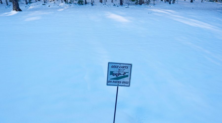 Golf carts on paths only signage alongside the path in a snow covered golf course in the shade in wintertime